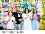 Семья с двумя детьми на вечеринке по случаю определения пола ребенка "Гендер пати". Они держат аксессуары, реквизит, бумажные усы и снимки УЗИ. Стоковое фото, фотограф Яна Проничева / Фотобанк Лори