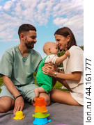 Young mom and dad hug and kiss their little daughter in the park on a picnic. Стоковое фото, фотограф Ярославский Максим / Фотобанк Лори