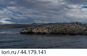 Many cormorants are sitting on a rocky island. Black and white seabirds on the cliffs. Ripples on the ocean surface. Clouds in the sky. Argentina. Tierra del Fuego Archipelago. The Beagle Channel. Стоковое фото, фотограф Вера Ивановна Кубарева / Фотобанк Лори