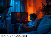 Ребенок сидит один в темной комнате, смотрит фильм по телевизору. Стоковое AI-изображение, AI-художник Щеголева Ольга / Фотобанк Лори