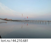 Водная гладь на стилобате Лахта Центра в Санкт-Петербурге, в которой отражается небо на закате, три флага (имперский, СССР и России) и облака (2024 год). Редакционное фото, фотограф Елена Яворская / Фотобанк Лори
