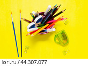 Pencils fluster brushes scissors and other office supplies in organizer glass on a yellow background. Стоковое фото, фотограф Дмитрий Львович Алферов / Фотобанк Лори