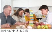 Elderly man engrossed in playing jenga with wife, adult son and daughter-in-law during fun family gathering with wine at home, concentrating on extracting block without collapsing tower. Стоковое видео, видеограф Яков Филимонов / Фотобанк Лори
