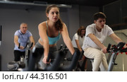 Concentrated young fit girl working out on stationary bicycle in gym. Healthy active lifestyle concept. Стоковое видео, видеограф Яков Филимонов / Фотобанк Лори