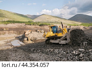 Японский Бульдозер Komatsu D375 в горной местности,сгребает от промывочного устройства отработанный горный грунт, чтобы затем его сгрести ковшом в отвал. На дальнем плане - стационарное промывочное устройство для промывки золота (2009 год). Редакционное фото, фотограф Павел Просянов / Фотобанк Лори