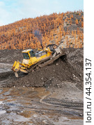 Бульдозер Komatsu D -375  в горной местности сгребает кучу горного золотосодержащего грунта , который колесным погрузчиком Komatsu WA500 будет перевозиться на промывку с целью извлечения желтого драгоценного метала (2009 год). Редакционное фото, фотограф Павел Просянов / Фотобанк Лори