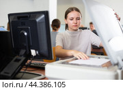 Focused female student using PC and xerox while studying computer science in the classroom. Стоковое фото, фотограф Яков Филимонов / Фотобанк Лори