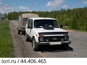 Белая нива с легковым прицепом стоит на загородной дороге. (2024 год). Редакционное фото, фотограф Фотиния Куимова / Фотобанк Лори