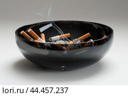 Extinguished cigarettes in black ashtray. Стоковое AI-изображение, AI-художник Иван Рябоконь / Фотобанк Лори