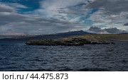 A small rocky island in the Beagle Channel. Cormorants are sitting on cliffs. Seabirds are flying. The Andes mountain range is on the horizon. Clouds in the blue sky. Argentina. The Beagle Channel. Стоковое фото, фотограф Вера Ивановна Кубарева / Фотобанк Лори
