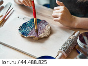 Unrecognised Woman making pattern on ceramic plate, hands close-up, focus on palms with paint brush. Creative hobby concept. Earn extra money, side hustle, turning hobbies into cash, passion into job. Стоковое фото, фотограф Natalia Gdovskaia / Фотобанк Лори