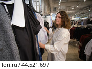 Person browsing clothing racks in a fashion retail store. Indoor candid shot in a shopping environment. Стоковое фото, фотограф Андрей Журавлев / Фотобанк Лори