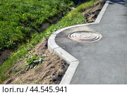 Lateral curve of an asphalt sidewalk designed to accommodate a manhole cover, illustrating urban infrastructure's functional and aesthetic integration in cityscapes. Стоковое фото, фотограф Татьяна Степанищева / Фотобанк Лори