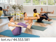 Young woman coach and students perform Paripurna Navasana during training in studio. Стоковое фото, фотограф Яков Филимонов / Фотобанк Лори