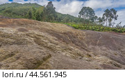 The amazing 23 colored earth of Mauritius. A hill of multicolored sand in the foreground. Green vegetation in the distance. A mountain against a blue sky, clouds. La Vallée Des Couleurs Nature Park (2024 год). Стоковое фото, фотограф Вера Ивановна Кубарева / Фотобанк Лори
