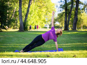 Woman leading a healthy lifestyle, doing yoga in the park, doing Vasishthasana exercise, side plank pose on outstretched arms, training alone in sportswear on a mat. Стоковое фото, фотограф Сергей Чайко / Фотобанк Лори