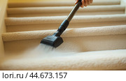 Person using a vacuum cleaner to clean carpeted stairs in a well-lit indoor setting during the daytime. Стоковое AI-изображение, AI-художник Сергей Толмачёв / Фотобанк Лори