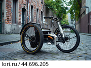 Modern three wheeled recumbent bike parked on cobblestone street. Стоковое AI-изображение, AI-художник Иван Рябоконь / Фотобанк Лори
