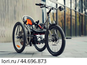 Modern three wheeled electric recumbent bicycle parked in urban environment. Стоковое AI-изображение, AI-художник Иван Рябоконь / Фотобанк Лори