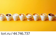 Various hot coffees in ceramic cups lined up on a yellow background. Стоковое AI-изображение, AI-художник Veniamin Kraskov / Фотобанк Лори