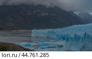 The famous Perito Moreno Glacier. A wall of cracked blue ice above a glacial lake. Melted ice floes float in the water. Coastal mountains in clouds and fog. El Calafate. Lago Argentino. Argentina. Стоковое фото, фотограф Вера Ивановна Кубарева / Фотобанк Лори