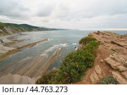 Breathtaking seascape in Basque Autonomous Community / country in gloomy summer day. Atlantic ocean beach Algorri surrounded by mountains at low tide in Bay of Biscay. Layers of flysch on the coast at Zumaia. Стоковое фото, фотограф YuryKara / Фотобанк Лори