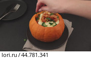Whole baked pumpkin with tiger prawns, melted cheese and tomatoes. The woman adds parsley. Traditional dish of Brazil, home cooking. Selective focus, close-up, black background. Стоковое видео, видеограф Наталья Любина / Фотобанк Лори