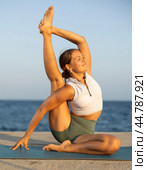 On windy day young slender woman does yoga near sea doing Parivritta Surya Yantrasana. Стоковое фото, фотограф Яков Филимонов / Фотобанк Лори