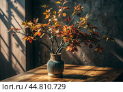 Branches with golden autumn leaves in a ceramic vase on a wooden table by the window. The concept of home comfort. Autumn decor for Halloween. Стоковое AI-изображение, AI-художник Photojuli / Фотобанк Лори