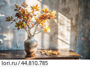 Branches with golden autumn leaves in a ceramic vase on a wooden table by the window. The concept of home comfort. Autumn decor for Halloween. Стоковое AI-изображение, AI-художник Photojuli / Фотобанк Лори