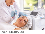 Young female client receiving hardware ultrasonic to revitalize and tighten facial skin at clinic. Стоковое фото, фотограф Яков Филимонов / Фотобанк Лори