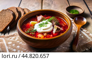 Сытная тарелка традиционного русского борща, украшенная сметаной и укропом, подается с ржаным хлебом на деревенском столе. Стоковое AI-изображение, AI-художник Константин Сигаев / Фотобанк Лори