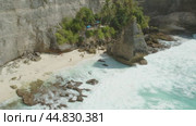 Aerial view of Diamond Beach in Nusa Penida, showcasing a small secluded sandy cove with tourists exploring near rocky cliffs. Стоковое видео, видеограф Ольга Сухарева / Фотобанк Лори