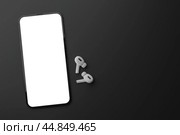 Phone with blank white screen and wireless headphones. Mockup cellphone and TWS earbuds on black background. Audio technology apps, music podcasts books. Стоковое фото, фотограф Павел Муравьев / Фотобанк Лори