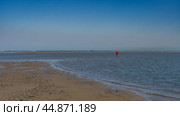 The time of low tide. A woman walks through the shallow water with a plastic bucket. The ocean is ahead. On the exposed sandy seabed there is a pattern of sandy ridges and puddles of water. Стоковое фото, фотограф Вера Ивановна Кубарева / Фотобанк Лори