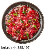 Thinly sliced beef carpaccio with arugula and sesame seeds on black plate. Стоковое AI-изображение, AI-художник Иван Рябоконь / Фотобанк Лори