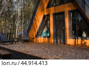 A-shaped frame house in Scandinavian style. The landscape. Quiet rest. The concept of glamping and chalet rentals. A wooden house with a veranda in nature around an autumn birch forest. Стоковое фото, фотограф Photojuli / Фотобанк Лори