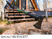 An axe will be stuck into a wooden log. Harvesting firewood for the winter season. Logging on the background of a country house. Lumber, wood-cutting tools. Стоковое фото, фотограф Photojuli / Фотобанк Лори