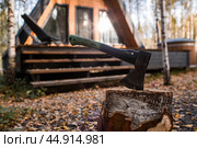 An axe will be stuck into a wooden log. Harvesting firewood for the winter season. Logging on the background of a country house. Lumber, wood-cutting tools. Стоковое фото, фотограф Photojuli / Фотобанк Лори