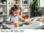 Toys. A little girl is playing educational games. A rainbow-shaped children's toy, colored pyramids and logic toys for children. Montessori games for child development. Стоковое AI-изображение, AI-художник Photojuli / Фотобанк Лори