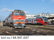 Тепловоз 2ТЭ116УД и дизель-поезд РА3 "Орлан" на железнодорожной станции  солнечным августовским днем. Рыбинск (2024 год). Редакционное фото, фотограф Виктор Карасев / Фотобанк Лори