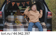 A little girl is sitting in the trunk of a car and wearing a witch hat for the Halloween holiday. The concept of children's Halloween. Стоковое видео, видеограф Терехова Марина / Фотобанк Лори