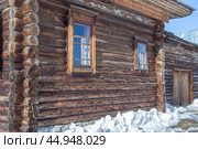 Деревянный дом из оцилиндрованного бревна в поселке Хохловка. Отреставрированный деревенский дом, построенный в 19 веке. Потрескавшиеся темные бревна деревянного дома. Сугробы снега зимой возле дома в сельской местности. (2024 год). Стоковое фото, фотограф Эдуард Белкин / Фотобанк Лори