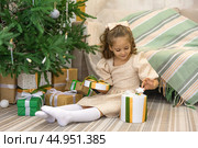 Christmas spirit. Happy little smiling girl opening gift box sitting on the floor near the Christmas tree. Happy girl unwrapping Christmas present looking in box. Holidays and celebrations concept. Стоковое фото, фотограф Ирина Михайличенко / Фотобанк Лори