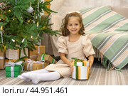 Christmas spirit. Happy little smiling girl opening gift box sitting on the floor near the Christmas tree. Happy girl unwrapping Christmas present looking in box. Holidays and celebrations concept. Стоковое фото, фотограф Ирина Михайличенко / Фотобанк Лори