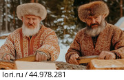 Русская традиция: мужчины в меховых шапках рубят дрова зимой для сезонных плакатов. Стоковое AI-изображение, AI-художник ФотоИнтеллект / Фотобанк Лори
