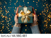 A woman holds a gift box with a gold satin ribbon bow on an emerald green background with a beautiful side. Стоковое AI-изображение, AI-художник Photojuli / Фотобанк Лори