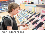 11-летний мальчик с рюкзаком выбирает себе мобильный телефон в магазине техники. Стоковое фото, фотограф Яна Проничева / Фотобанк Лори