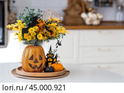 A vase of flowers, pumpkins and a scary castle with a witch on the background of a Scandi-style white kitchen interior. The concept of home and comfort. Autumn decor for Halloween. Стоковое фото, фотограф Photojuli / Фотобанк Лори