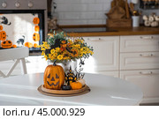 A vase of flowers, pumpkins and a scary castle with a witch on the background of a Scandi-style white kitchen interior. The concept of home and comfort. Autumn decor for Halloween. Стоковое фото, фотограф Photojuli / Фотобанк Лори